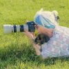 Woman with blue and white hair taking photos with a camera in a grassy field.