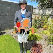 Young equestrian rider with ribbons and trophy in garden setting.