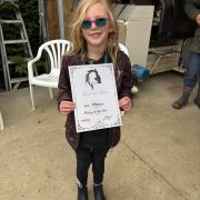 Young girl with sunglasses holding a certificate outdoors.