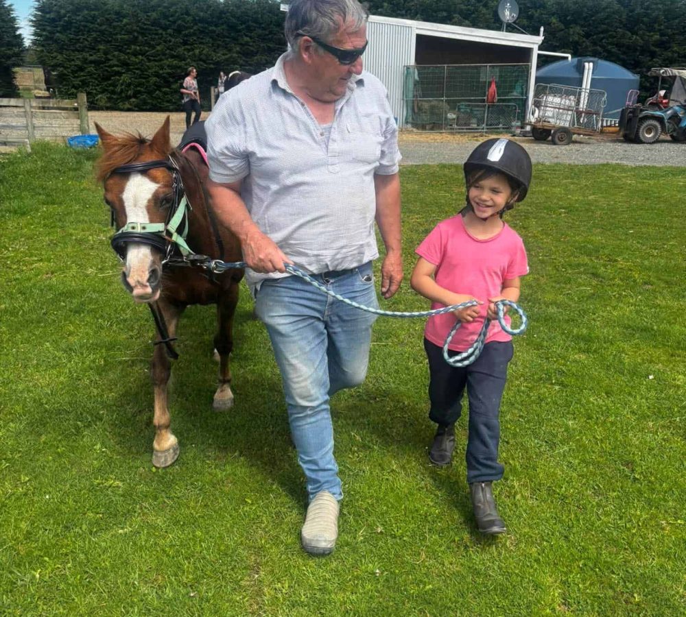 Man and girl walking a pony on a grassy field at Reigning Downs Hauora Centre.